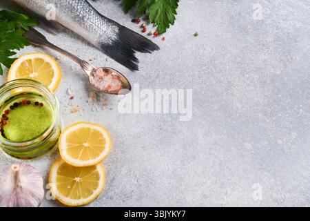 Pesce fresco. Branzino crudo con sale, pepe, prezzemolo, olio d'oliva e limone sul tagliere su fondo rustico in cemento grigio chiaro Foto Stock