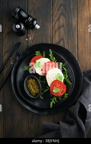 Insalata caprese. Insalata caprese italiana con pomodori a fette, mozzarella, rucola, basilico, olio d'oliva in piatto nero troppo vecchio Foto Stock