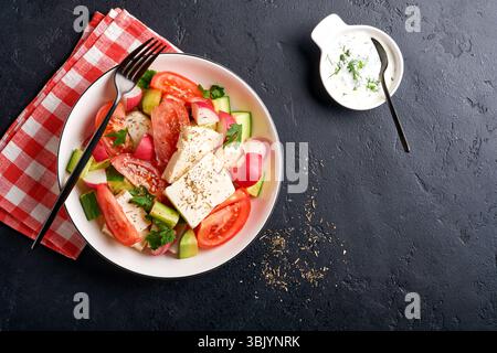 Ravanello, cetriolo, pomodoro, pepe e formaggio feta con spezie pepe e olio d'oliva in un recipiente bianco su ardesia nera, pietra o cemento Foto Stock