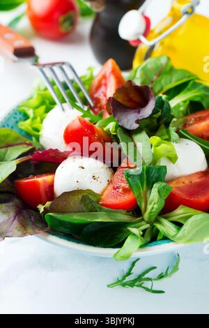 Insalata fresca con lattuga, insalata di salsa, rucola, barbabietole, pomodori, formaggio mazarella e olive in una tazza di ceramica su un retrogro leggero Foto Stock