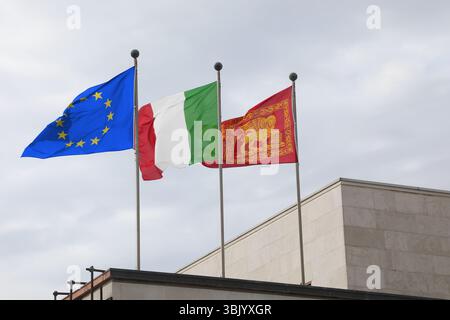 Venezia, VE, Italia - 6 maggio 2025: Tre bandiere d'Europa blu con stelle gialle e italiane e bandiera della regione Veneto con leone alato Foto Stock