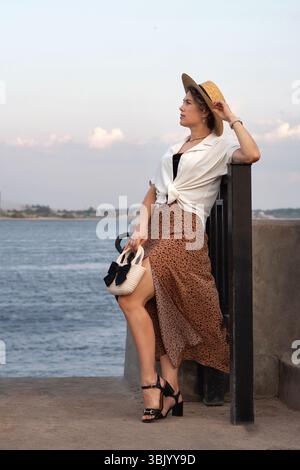 Donna in abito estivo che posa accanto alla ringhiera del fiume Foto Stock