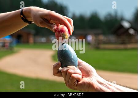 Le uova colorate vengono bilanciate precariamente da due mani in un'area verde del parco. Foto Stock