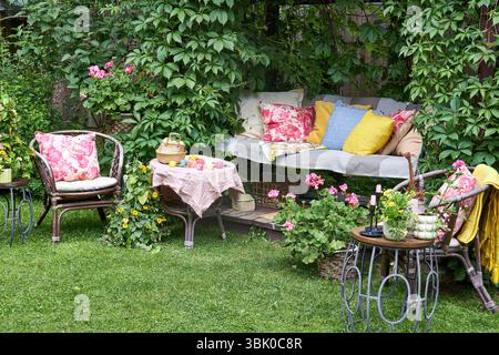 Un accogliente angolo esterno per la creatività in un giardino estivo: Un'altalena imbottita funge da posto rilassante per il ricamo, circondato da una vegetazione lussureggiante e. Foto Stock