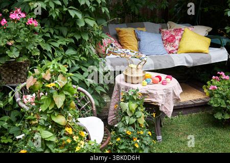 Un accogliente angolo esterno per la creatività in un giardino estivo: Un'altalena imbottita funge da posto rilassante per il ricamo, circondato da una vegetazione lussureggiante e. Foto Stock