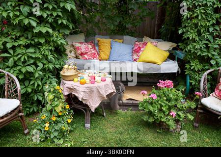 Un accogliente angolo esterno per la creatività in un giardino estivo: Un'altalena imbottita funge da posto rilassante per il ricamo, circondato da una vegetazione lussureggiante e. Foto Stock