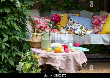 Un accogliente angolo esterno per la creatività in un giardino estivo: Un'altalena imbottita funge da posto rilassante per il ricamo, circondato da una vegetazione lussureggiante e. Foto Stock