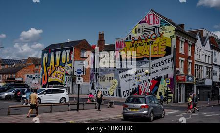 LEICESTER, Regno Unito - 14 GIUGNO 2025 - i pedoni godono di una giornata di sole vicino a colorati poster vintage che promuovono il Savoy Palace e altri luoghi di Leicester, U Foto Stock