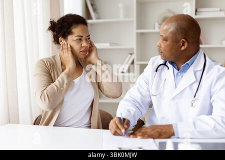 Medico maschio afroamericano che ascolta la donna nera millennial che descrive il dolore all'orecchio Foto Stock