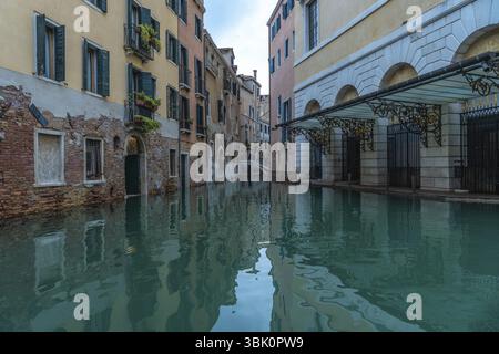 L'acqua calma riflette gli edifici colorati lungo un canale di venezia, in italia, durante l'acqua alta o l'alta marea Foto Stock