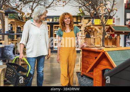 Venditore sorridente che mostra le casette dei cani in legno al cliente che porta il carrello in un negozio di animali Foto Stock