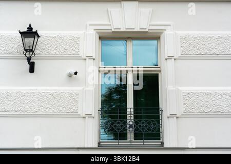 Facciata moderna di un edificio bianco con elementi decorativi classici, lampada da strada vintage, telecamera a circuito chiuso di sicurezza e finestra Foto Stock