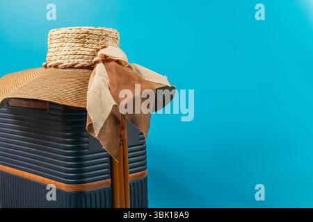 Un elegante cappello di paglia si appoggia elegantemente su una valigia blu, accompagnata da un morbido nastro. Perfetto per le avventure estive e la pianificazione di una fuga. Foto Stock
