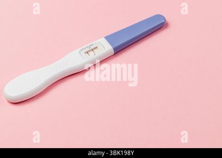 Un test di gravidanza visualizza due righe che indicano un risultato positivo. Il test viene posizionato su uno sfondo rosa tenue, evidenziandone le caratteristiche. Foto Stock