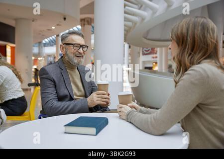 Un uomo maturo e una giovane donna che si godono un caffè e chiacchierate vivaci in un centro commerciale Foto Stock