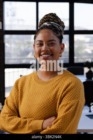 Donna sicura di sé in maglione giallo sorridente in un moderno ambiente ufficio Foto Stock