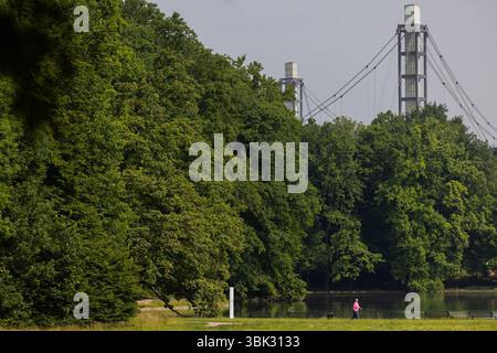 Colonia, Germania. 18 giugno 2025. Una donna nordic walking allo stagno Adenauer Weiher nella foresta cittadina sullo sfondo del RheinEnergieStadion. Crediti: Rolf Vennenbernd/dpa/Alamy Live News Foto Stock