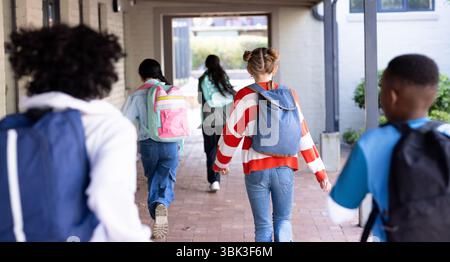 Diversi studenti che camminano insieme con gli zaini nel corridoio della scuola, godendosi la giornata Foto Stock