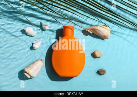 Bottiglia di crema solare e conchiglie in acqua su sfondo blu Foto Stock