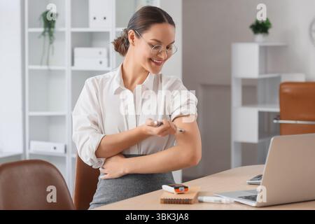 Giovane donna d'affari incinta con diabete gestazionale che usa una penna a lancetta a tavola in ufficio Foto Stock