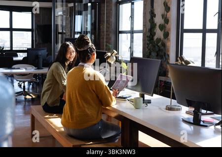 Donne diverse che collaborano a progetti di codifica in un ufficio moderno, condividono idee e sorridono, a casa Foto Stock