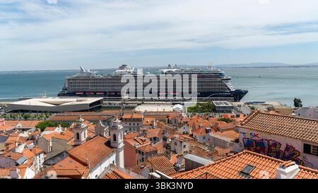 Lisbona, Portogallo - 22 maggio 2025: Gigantesca nave da crociera ancorata nel porto di Lisbona, incorniciata dagli iconici edifici dal tetto rosso della città e dallo storico skyline Foto Stock