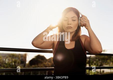Una donna serena con gli occhi chiusi ascolta musica rilassante o una meditazione guidata sulle cuffie, godendoti un momento di pace all'aperto Foto Stock