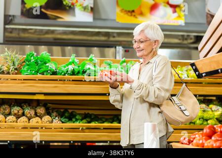 Donna anziana che tiene due pomodori rossi e li esamina nella sezione prodotti del supermercato, spazio copia Foto Stock