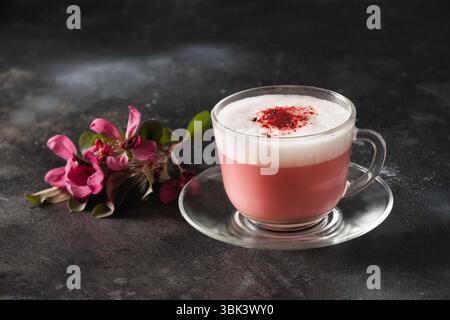 Latte matcha rosa con fiori sakura decorati a polvere su sfondo nero. Bevanda vegana alternativa alla moda. Primo piano. Foto Stock