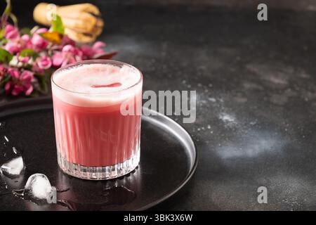 Latte matcha rosa con fiori sakura decorati a polvere su sfondo scuro. Bevanda alla moda. Rinfrescante matcha rosa ghiacciato. Primo piano. Foto Stock