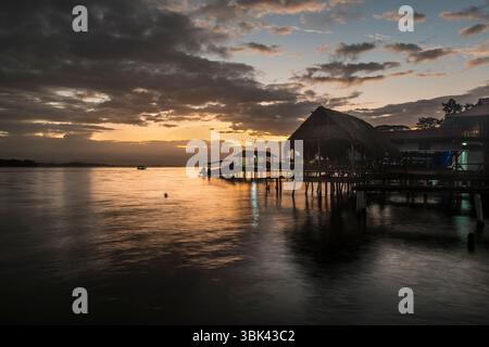 Vista al tramonto delle palafitte e di una barca ormeggiata presso la città vecchia, Isla Bastimentos, Bocas del Toro, Panama Foto Stock