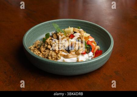 Una colorata ciotola per brunch piena di yogurt, frutta fresca e granuli croccanti si trova su un tavolo di legno, che offre una colazione nutriente e appetitosa. Foto Stock