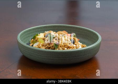 Una variopinta ciotola di muesli condita con frutta fresca e noci si siede su un tavolo di legno e offre una salutare opzione per la colazione. Foto Stock