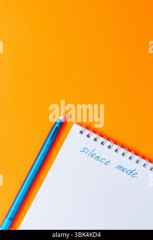 Blocco appunti con la modalità silenziosa frase e una penna blu su sfondo arancione brillante. Scuola di arte pop o ufficio di cancelleria. Foto Stock