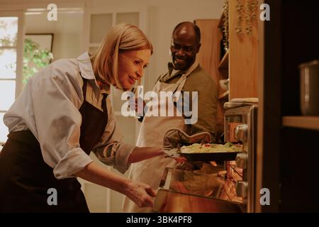 Donna caucasica anziana e uomo nero anziano che cucinano insieme in cucina sorridendo Foto Stock