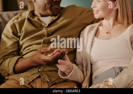 Coppia multietnica anziana seduta insieme tenendosi per mano e sorridendo Foto Stock