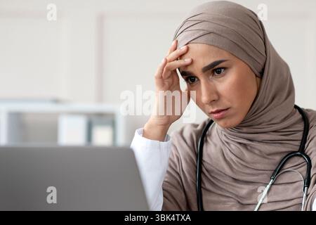 Stanco medico femminile che ha mal di testa mentre lavora con il computer portatile Foto Stock