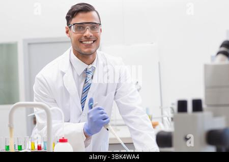 Scienziato maschio in camice da laboratorio pipettando liquidi in rack per provette con micropipetta al banco di laboratorio Foto Stock