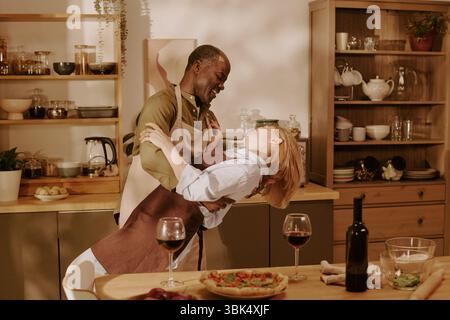 Coppia multietnica senior che ballano insieme in cucina per celebrare il romanticismo Foto Stock