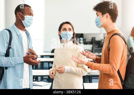 Felici studenti internazionali che indossano maschere mediche e parlano Foto Stock