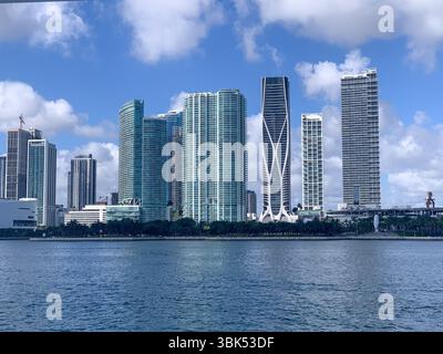 Una vibrante vista del centro di Miami, Florida, con eleganti e moderni grattacieli lungo il lungomare di Biscayne Bay, sotto un cielo blu brillante con nuvole Foto Stock