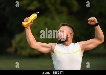 Un giovane uomo felice in forma che alza il pugno dopo un allenamento di successo. Concetto di trionfo sportivo, vittoria. Foto Stock