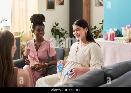 Donna caucasica in gravidanza con stivaletti blu seduti con una giovane donna nera adulta sorridente e un'altra giovane donna caucasica adulta Foto Stock