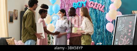 Gruppo di giovani adulti e donne multietniche di mezza età in piedi insieme sorridendo e tenendo regali alla festa di rivelazione di genere Foto Stock