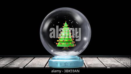 Mostra il globo della neve su un tavolo in legno che mostra l'albero con la stella garland e le baule rosse Foto Stock