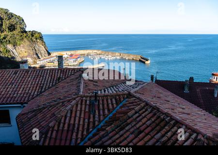 Villaggio costiero visto dall'alto, con tetti in terracotta e un tranquillo porto pieno di barche. Lastres, Asturie Foto Stock