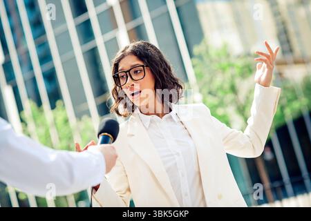 Donna d'affari sicura che parla all'aperto di successo e leadership, indossa abiti formali, in un ambiente urbano moderno Foto Stock
