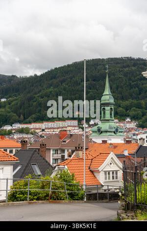 Vista panoramica della vecchia guglia della chiesa e dei tetti piastrellati contro la foresta di Bergen, Norvegia Foto Stock