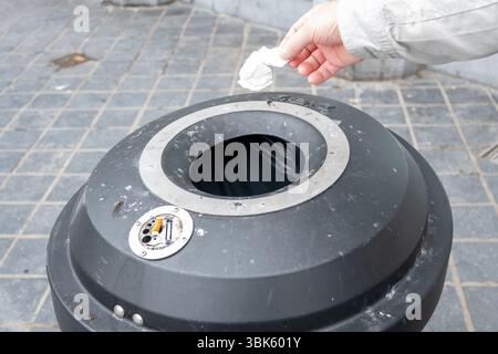 Persona che lancia un tovagliolo di carta schiacciato nel cestino della spazzatura. Barattolo di metallo per strada. Igiene in città. Foto Stock