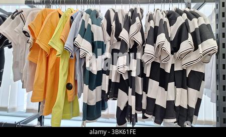 Magliette colorate e a righe appese su rack in una stanza illuminata dal sole Foto Stock